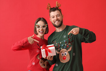 Happy young couple in stylish Christmas clothes and with gift on color background