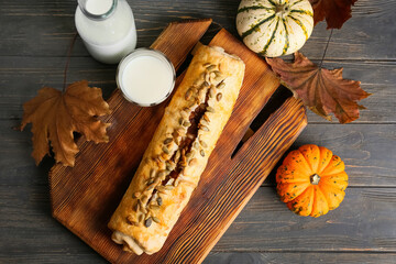 Board with tasty pumpkin strudel and glass of milk on wooden background
