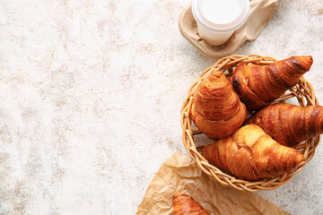 Wicker basket with delicious croissants on light background