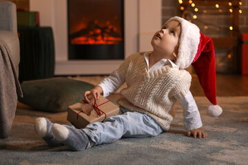 Obraz premium Little boy in Santa hat and with Christmas gift at home