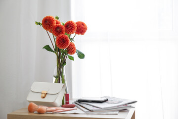Vase with beautiful dahlias, female accessories, cosmetics and magazines on table in room