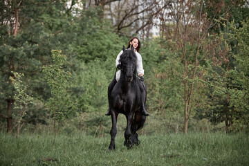 Beautiful long-haired girl riding a Friesian horse