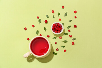 Composition with cup of tasty lingonberry tea and berries on green background