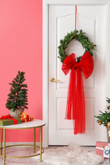 White door with decor and table with Christmas tree near color wall