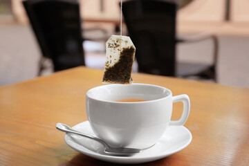 Dipping of tea bag into cup on table