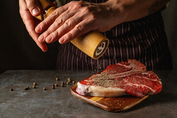 The hands of the chef add fresh pepper from the mill to the beef steak