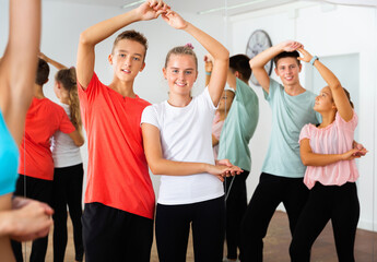 Group of happy cheerful positive teenage boys and girls training movements of slow foxtrot in dance...