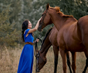 Obraz premium Beautiful long-haired girl in a blue dress next to two horses