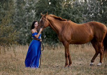 Beautiful long-haired girl in a blue dress with a red horse