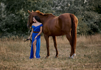 Fototapeta premium Beautiful long-haired girl in a blue dress with a red horse