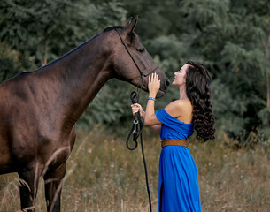 Beautiful long-haired girl in a blue dress with a brown horse