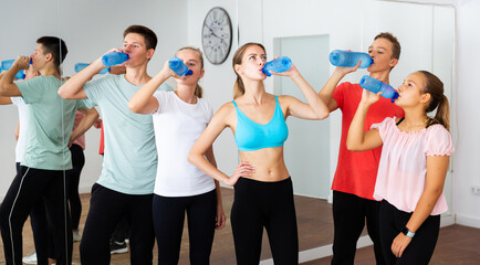 Group of teenagers taking break during dance class, drinking bottled water with their young female teacher