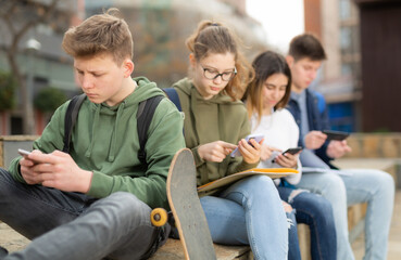 Teenage schoolers boys and girls using their gadgets outside on sunny day