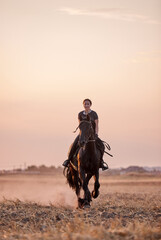 Girl riding a friesian horse in a field at sunset