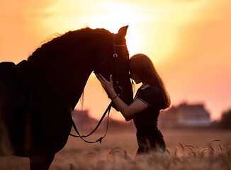 A girl next to a friesian horse at sunset in a field