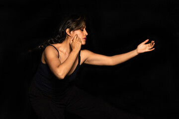 Side shot of a Latina woman with indigenous features extending her hands to the front while having a dramatic expression on a black background