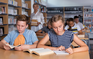 Fototapeta premium Schoolchildren preparing for lesson in school library, reading textbooks