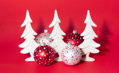 Christmas card with snow-covered white New Year trees and colorful balls on bright red background.