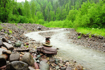 A small cairn on the bank of a turbulent mountain river flowing through a summer forest after a rain.