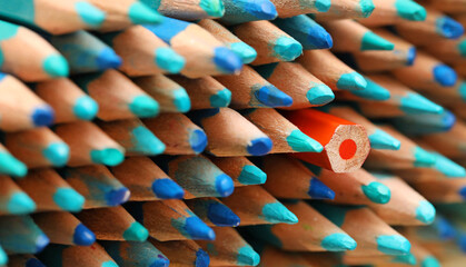 A single orange colored pencil pointing in the opposite direction to the large quantity of sharp...