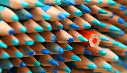 A single orange colored pencil pointing in the opposite direction to the large quantity of sharp blue pencils. Standing out in the crowd or being different concept. Individuality