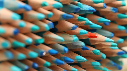 A single sharp orange colored pencil pointing in the opposite direction to the blue pencils....