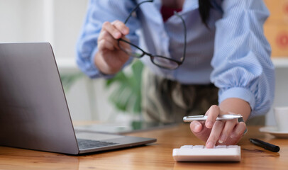 Close up Business woman using calculator and laptop for do math finance on wooden desk in office and business working background, tax, accounting, statistics and analytic research concept