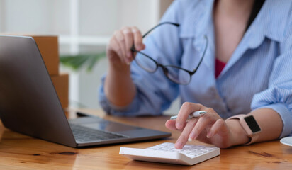 Close up Business woman using calculator and laptop for do math finance on wooden desk in office and business working background, tax, accounting, statistics and analytic research concept