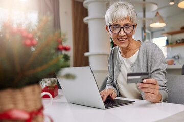 an elderly woman wearing glasses is sitting at home buying Christmas presents