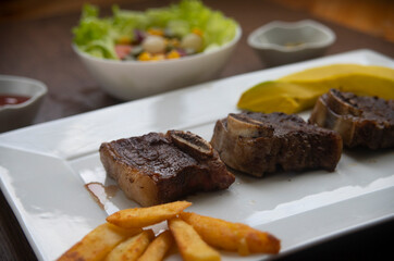 ROASTED BEEF, SERVED ON A WHITE PLATE AND LETTUCE, TOMATO AND CORN SALAD, ACCOMPANIED WITH FRENCH FRIES AND AVOCADO