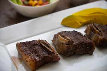 ROASTED BEEF, SERVED ON A WHITE PLATE AND LETTUCE, TOMATO AND CORN SALAD, ACCOMPANIED WITH FRENCH FRIES AND AVOCADO