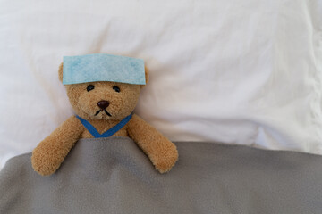 Teddy bear lying sick in bed. Teddy bear with antipyretic patch