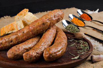 The photograph shows many salami on a wooden board next to a piece of bread, cutlery and some spices.