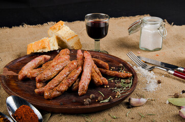 The photograph shows many salami on a wooden board next to a piece of bread, cutlery and some spices.