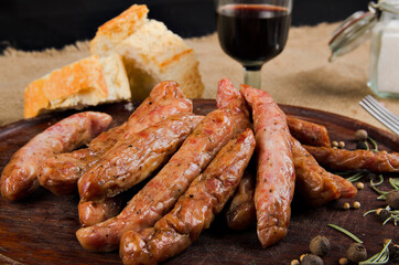 The photograph shows many salami on a wooden board next to a piece of bread, cutlery and some spices.
