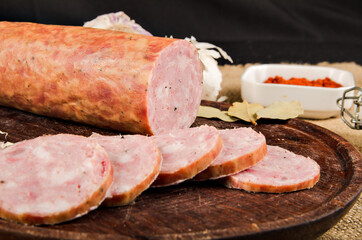 The photograph shows a quite appetizing salami, sliced on top of a wooden board with some spices.