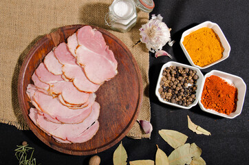 the photograph shows some pieces of ham cut into slices on top of a wooden board with some pieces of bread and some spices