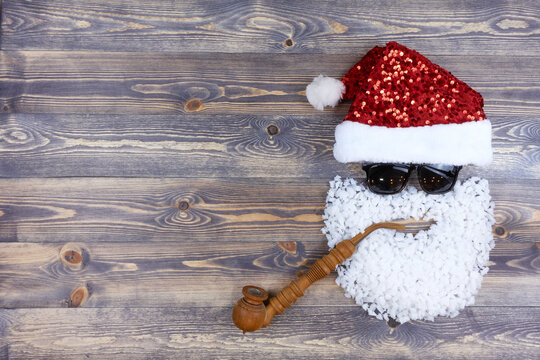 Head of Santa Claus in black glasses and with a smoking pipe on a dark wooden background. Winter landscape with copy space.