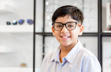 Smiling Indian-thai boy choosing glasses in optics store, Portrait of Mixed race ethnicity kid...