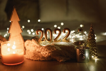 Happy New Year 2022. Number 2022 made by candles on a festive sparkling bokeh background in the dark. New Year background with sweaters, garlands and New Year decorations.
