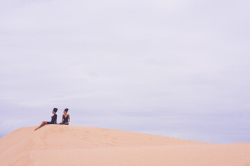 Two woman seen sitting on edge of sand dune