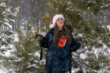 young woman in santa hat with christmas ball in winter in forest