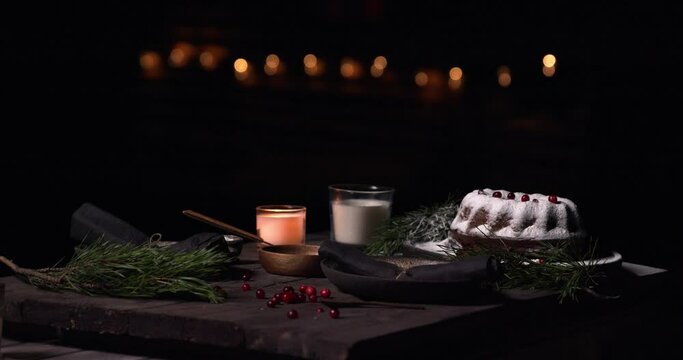 Isolated dark food christmas table set with candles, dessert cake with cream of tartar powder, pine leaves and red berries fruits