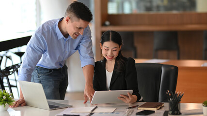 Businesswoman talking and working on tablet with caucasian male boss