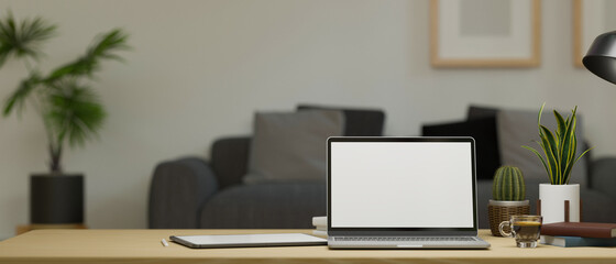 Modern working desk with laptop mockup and supplies over blurred comfy living room background.