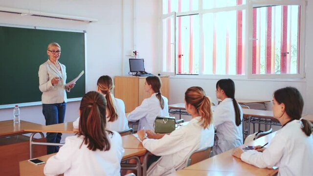 Group of medical students attentively listening to lecture of female teacher in classroom
