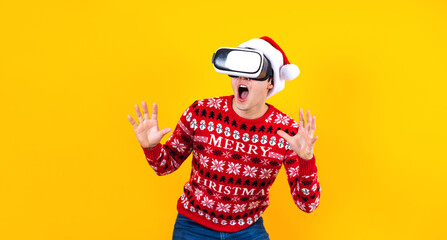 young latin man gamer in virtual reality headset gadget wearing Santa hat and Christmas sweater on yellow background. Christmas and winter vr technology concept in Mexico Latin America