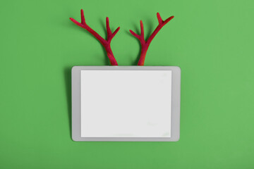 White touchpad with blank touchscreen with fake toy antlers of a deer on a red background. Merry Christmas or Happy New Year concept with space for your copy