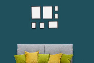 Turquoise wall of the room with empty frames and sofa.