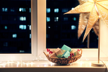 Christmas room decor. Basket with gifts, star night light and garland glow on the night window